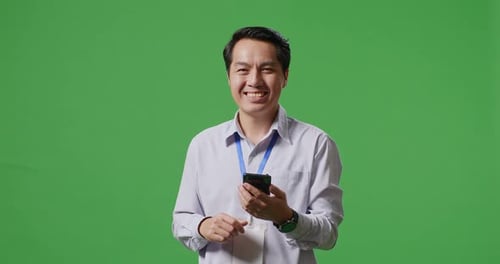 An Asian Business Man Using Mobile Phone And Smiling To Camera On Green Screen Studio