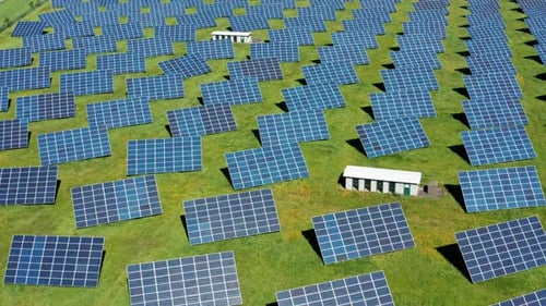 A vast solar farm with numerous panels on green fields under a clear blue sky