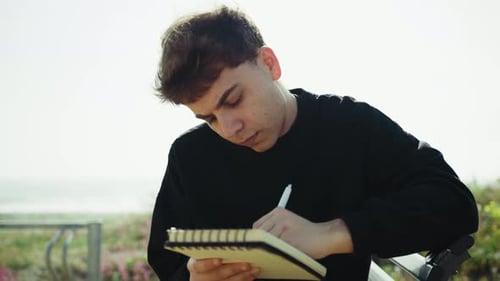 Man Writing Ideas On A Notebook With A Pen On A Park Bench