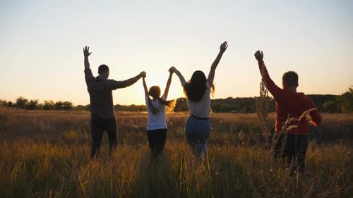 Mother and Father with Two Small Children Jog Through Grass Field with Raising Hands at Sunset Happy