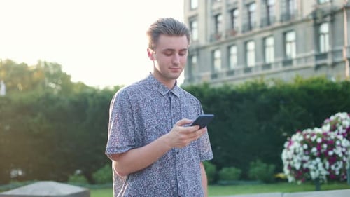 Joyful Caucasian Young Man Texting on Smartphone While Walking in Town Handsome Guy Smiling While