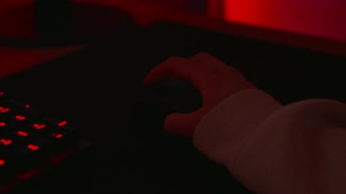Anonymous hacker in a dark red room using a mouse.