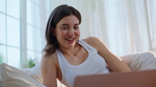 Brünette spricht virtuelles Meeting am Laptop und entspannt sich im bequemen Bett, Nahaufnahme