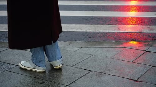 Closeup View of a Pedestrian at a Wet Crosswalk Waiting at the Curb As Red Signal Lights Reflect on