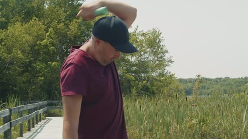Man Shields From Mosquitoes with Repellent Spray By the Lake