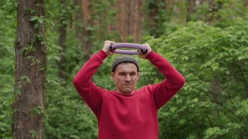 Um esportista profissional com uma camisa vermelha é visto segurando um expansor de anel roxo para Pilates enquanto