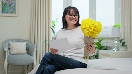 Woman Reading Letter With Yellow Bouquet Smiling Indoors