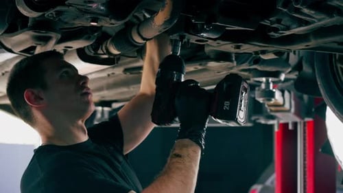 Close Up an Auto Mechanic at Service Station Checks a Car Being Lifted on a Lift Fixing Problems