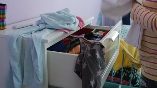 Child Organizes Clothing in Dresser Drawer at Home
