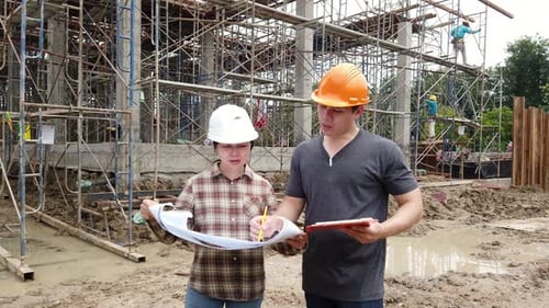 Construction manager and engineer discussing and checking plans on construction site.