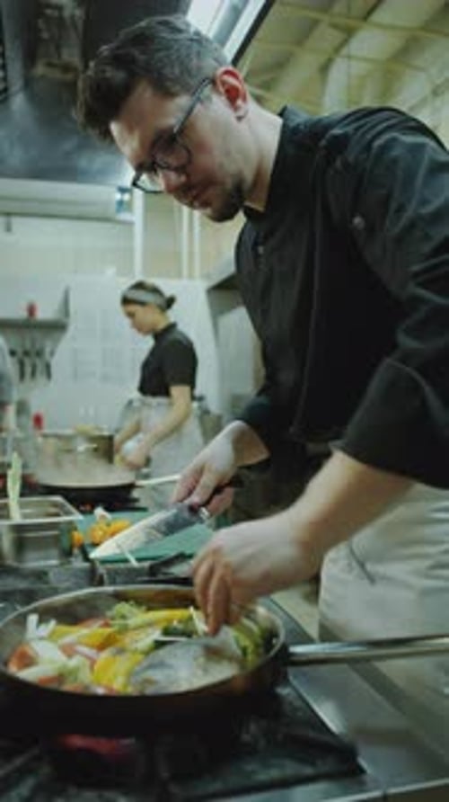 Restaurant Chef Adding Vegetables to Fish in Cooking Pan