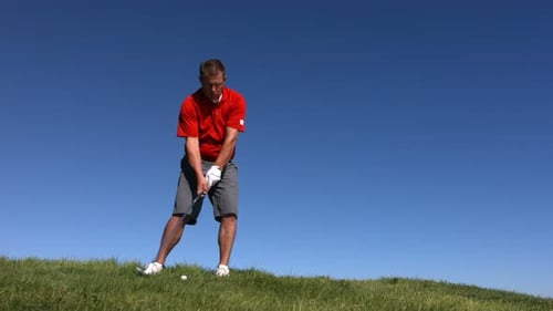 Man Swings Golf Club on Green Hill During Day