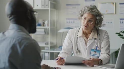 Middle-Aged Female Doctor Reading Medical History and Speaking with Patient