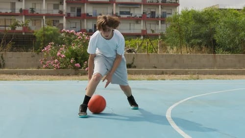 Teen Dribbling Basketball on Outdoor City Court