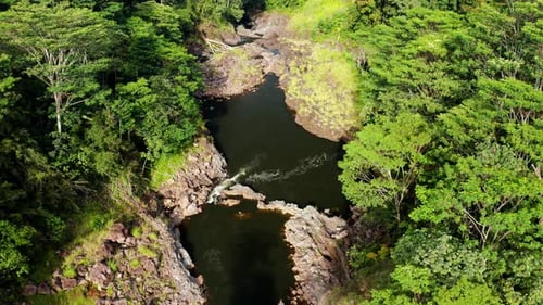 Aerial view of winding river gorge with rocky pools surrounded by dense rainforest