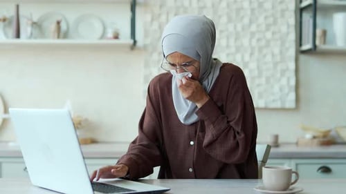 Young Woman Sneezing While Working on Laptop