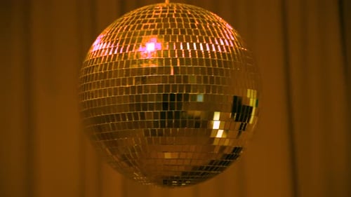 Disco ball spins under green lights at a lively dance event