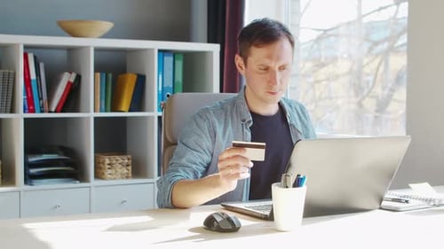 Young Man Makes Purchases on the Internet Using a Bank Credit Card The Person Works at Home at the