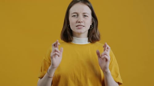 Slow Motion Portrait of Nervous Young Lady Crossing Fingers and Praying Against Yellow Color