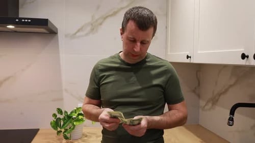 Man Counting Cash in Modern Kitchen During Evening Hours