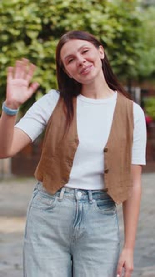 Cheerful Young Woman Smiling Friendly at Camera Waving Hands Gesturing While Standing on City Street
