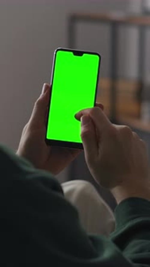 Person Holding Smartphone with Bright Green Chroma Key Screen Indoors Showcasing Blank Mobile
