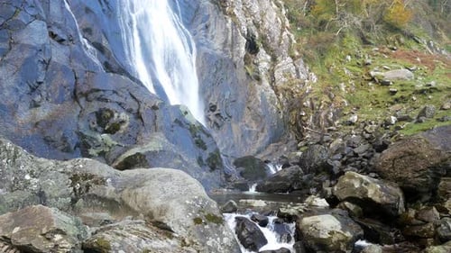 Rocky cascading waterfall flowing into jagged river rocks and boulders left dolly