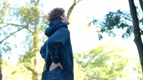 Back View Young Caucasian Man Massaging His Back in Green Park Between Trees Rear View Sportsman