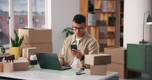 Young Adult Using Phone and Laptop at Desk