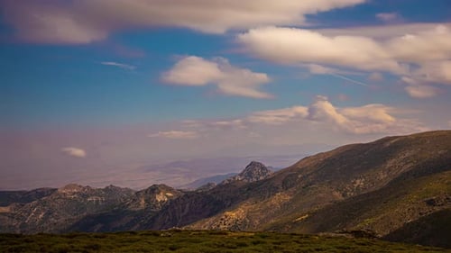 Shot of white clouds rapidly moving over green mountain range over blue sky in timelapse.