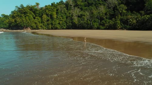 Woman in bikini jogs at waters edge on empty jungle beach in Costa Rica