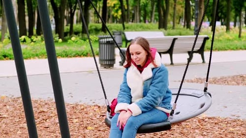 Une belle et joyeuse femme vêtue de vêtements chauds se balance sur une balançoire dans le parc