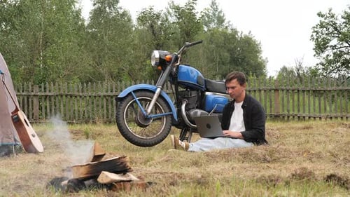Freelancer Working Remotely on Laptop Near Motorcycle at Campsite
