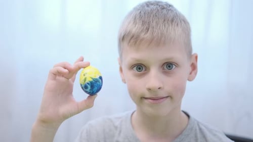 Easter Boy Holds in His Hand an Easter Egg Painted in Yellow and Blue Colors