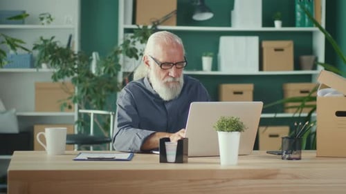 Concentrated Elderly Businessman Working Online While Sitting at His Desk