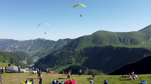 Gleitschirmflieger starten am Hang eines Berges, während andere ihre Ausrüstung aufbauen. Spect