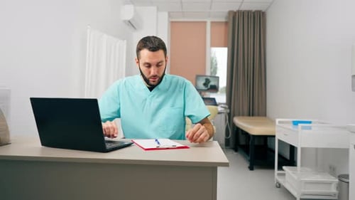 A doctor with a beard conducts an online consultation with a patient using laptop in his office