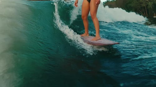 Female wake surfer's legs on pink board surfing perfect wave on lake in slow motion