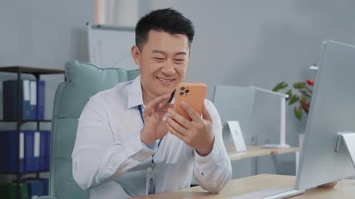 Man Uses Mobile Phone at Desk in Office