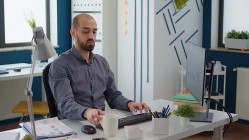 Man Typing on Computer Drinking Coffee in Office
