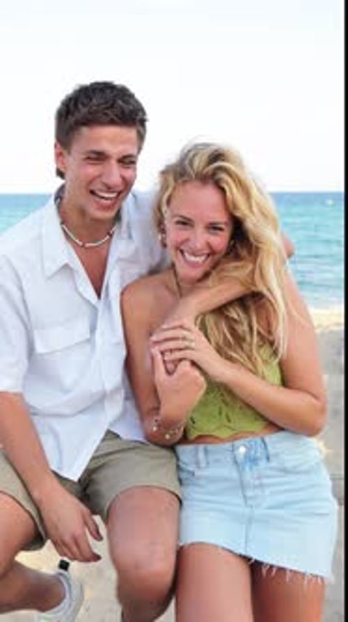 Joyful Couple Enjoying a Sunny Beach Day While Playfully Waving and Laughing By the Beautiful