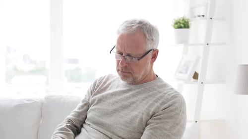 Senior Man Using Tablet on White Couch at Home