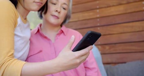 Granddaughter and Grandmother Look at Mobile Phone
