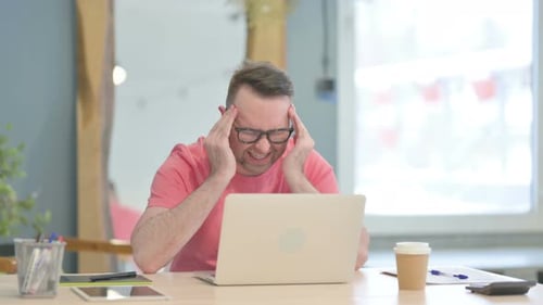 Man with Glasses Massaging Temples at Desk