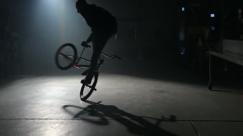 Young bmx rider performs extreme tricks in dark urban warehouse environment