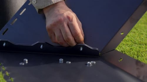 close-up of a Caucasian man's hand placing a screw into a dark, opaque metal support hole