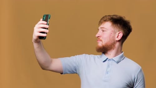 A Teenage Guy with a Big Smile on His Face Taking a Selfie with His Smartphone in a Studio