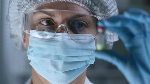 Healthcare Professional Holding Small Vial in Protective Gear