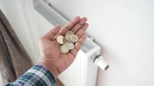 Münzen gegen Heizkörper zur Hand, um Energiekosten zu sparen