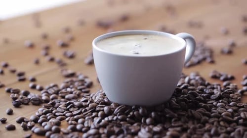 Coffee cup surrounded by coffee beans on wood